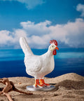 Decorative white chicken figure on sandy beach with ocean background