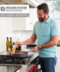 Man cooking with a nonstick pan in a modern kitchen, using a wooden spoon, showcasing the Slick Hardwire Smart Smoke And Carbon Monoxide Detector With Instant Phone Alerts Seamless Interconnection Reliable Battery Backup For Quick Setup And Rock Solid Home Safety Security.