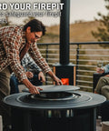 Person placing Surround Surface For Yukon Fire Pit Lid Durable Cold Rolled Steel Shield, 34.5 Inch Diameter, on a patio.
