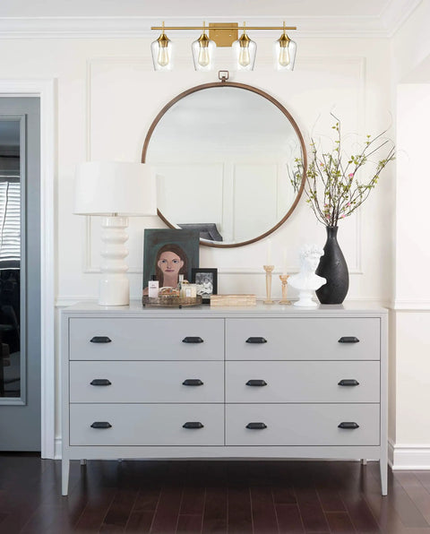 Industrial 4 Light Vanity Fixture With Clear Glass Bath Wall Sconces In Dope Gold Finish above a modern dresser and mirror in bathroom.