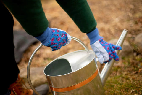 Soft Jersey Garden Gloves For Women Three Pack Assorted Colors Green Red Blue With Flower Print And Knit Wrist 100 Percent Cotton PVC Dots For Strong Grip And All Day Comfortable Gardening being worn while holding a watering can.