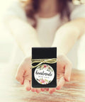 Black gift box with 'handmade with love' floral label on wooden table, presented by hands