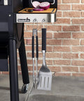 Precision 3 Piece Grilling Tool Set With Stainless Steel Tongs Spatula And Silicone Basting Brush hanging on the side of a grill
