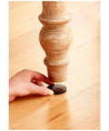 Applying brown felt furniture pad on wooden chair leg to protect hardwood floors from nicks, dents, and scratches.