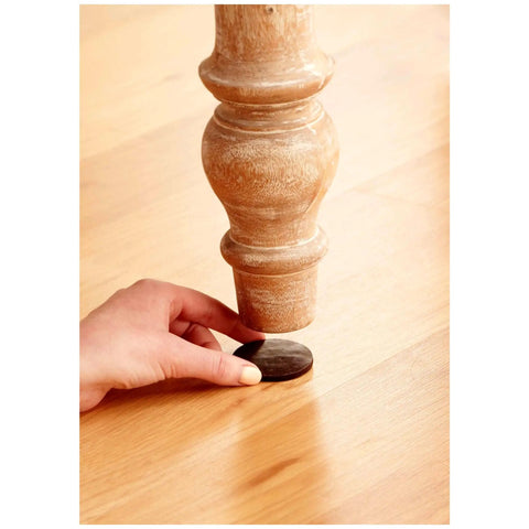 Applying brown felt furniture pad on wooden chair leg to protect hardwood floors from nicks, dents, and scratches.