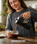 Woman pouring coffee from French Press Coffee Maker 20 Oz On The Go With Heat Resistant Borosilicate Glass And Stainless Steel 4 Level Filtration System Portable Cold Brew For Travel Camping Or Gift Black into a glass cup on a kitchen counter.