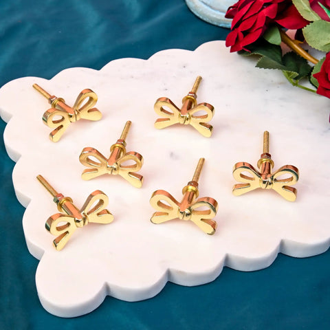 Set Of 8 Brass Bow Knobs For Cabinets And Drawers displayed on marble surface