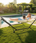 Freestanding Outdoor Hammock With Stand For Your Yard Deck Or Patio Built Tough With 600 Pound Capacity Rust Proof Stainless Steel Connectors Includes Soft Pillow And Handy Storage Bag White in a garden setting with woman relaxing