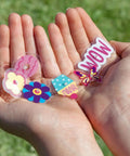 Hands holding colorful charms from Totally Adorable Kids Bike Spoke Decorations Set With 36 Colorful Charms Featuring Dino, Flower And Butterfly Themes.
