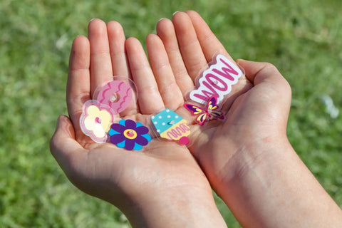Hands holding colorful charms from Totally Adorable Kids Bike Spoke Decorations Set With 36 Colorful Charms Featuring Dino, Flower And Butterfly Themes.
