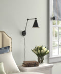 Vintage Adjustable Swing Arm Wall Lamp Black Dope Industrial Style Wall Sconce With Plug In Or Hardwired On Off Switch Ideal For Desk Or Bedside Reading Light in bedroom setting with bed and flowers.