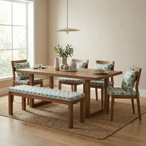Dining room with wooden table, chairs, and a bench featuring floral cushions. Sunlit window in background.