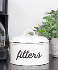 Basket Style White Enamel Coffee Filter Holder, The Go To Rustic Farmhouse Distressed Look, Shabby Chic Kitchen Organizer, next to a plant.