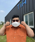 Person wearing Large White KF94 Disposable Mask With 4 Layer Filter and 3D Design in front of a building, adjusting the earloops.