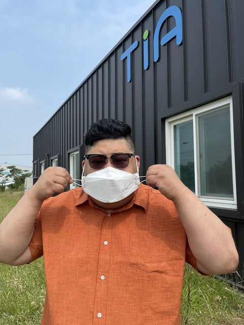 Person wearing Large White KF94 Disposable Mask With 4 Layer Filter and 3D Design in front of a building, adjusting the earloops.
