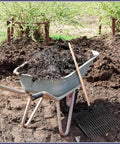 Beefy Pair Heavy Duty Horse Manure Fork Heads For 1 Inch Handles next to wheelbarrow filled with garden debris.