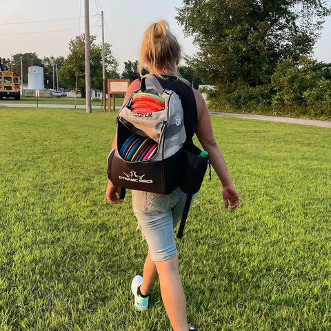 Person walking on grass wearing Trooper Disc Golf Backpack Holds 18 Plus Discs, Lightweight Yet Tough Bag For Beginners, Black.