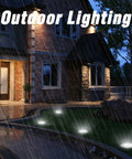 12 Pack Solar Ground Lights With 8 LED Each In Ground Round Puck Lights illuminate a rainy pathway by a house at night.