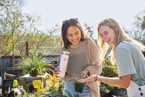 Two women outdoors, one holding AeroLight Transit Bottle 20 Oz With Locking Lid And Leak Resistant Design, Rose Quartz Glimmer color.