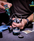 Marine Reel Care Kit With Oil And Grease For Freshwater And Saltwater Reels, showing oiler and grease syringe in use on fishing reel