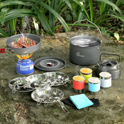 22 Piece Camping Cookware Mess Kit For Four With Hanging Pot Pan Kettle on ground for outdoor cooking setup.