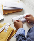 Person applying No Sweat White Mailing Address Labels For Slick Office Packing Feature Direct Thermal Printing to an envelope.