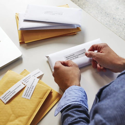 Person applying No Sweat White Mailing Address Labels For Slick Office Packing Feature Direct Thermal Printing to an envelope.