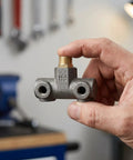 Hand holding Built Tough Cast Iron Four Way Air Compressor Manifold Fitting With One Half Inch And One Quarter Inch Male Threads