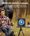 A man sitting by 11.5 Inch Portable Solar Powered Fan With Battery Backup For Camping Outdoor Travel Includes Solar Charger Timer And Lantern Perfect For Sleeping In Tents Cars Beaches Or During Hurricanes Keeps You Cool Anywhere