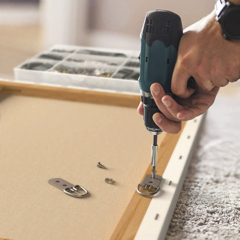 Person using a drill to attach D-ring from All In One Picture Hanging Kit With 100 Plus Pieces Including D Ring Screws Hooks Level And Stainless Steel Wire Hanger Supports Up To 50 Lbs 120 Feet Of Wire Comes In A Solid Box For Easy Do It Yourself Wall Art