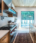 Modern kitchen interior with wooden cabinets and large window, featuring a patterned rug and sleek matte black cabinet hardware