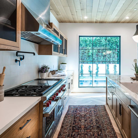 Modern kitchen interior with wooden cabinets and large window, featuring a patterned rug and sleek matte black cabinet hardware