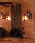 Rustic Wall Sconce Lantern With Glass Globe For Farmhouse Decor And Old School Vibe LED Five Point Five Watt Candle Light Electric Wall Light Fixture In Rust Finish With Authentic Oil Lantern Reproduction Style And Bottom Lit Glow next to fireplace with deer mounts in cabin setting