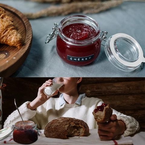 Glass jam jar with red cherry jam and metal clasp lid; croissant on wooden tray nearby.