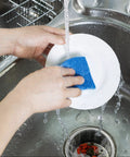 Person washing a plate in a sink using blue sponge above 500 Pcs Disposable Mesh Sink Strainer Bags Elastic Kitchen Filter Mesh Trash Bags Anti Clog Fits Most Strainer Sizes 3.9 x 4.3 Inch Keeps Your Sink Fresh And Odor Free For Quick No Mess Cleanups