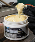 Gloved hand scooping Lith Ease White Lithium Grease 16 Oz Tub for heavy duty metal lubrication in workshop setting.