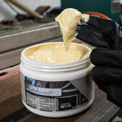 Gloved hand scooping Lith Ease White Lithium Grease 16 Oz Tub for heavy duty metal lubrication in workshop setting.