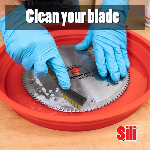Hands cleaning a saw blade in a red silicone tray with a wire brush, part of the Deluxe Saw Blade Cleaning Kit With Silicone Tray And 18oz Spray Cleaner Includes Trend Tool And Bit Cleaner Fulton Wire Brush Set And All In One Blade Care For Rust Removal And Mess Free Maintenance Up To 12 Inches Pro Grade.