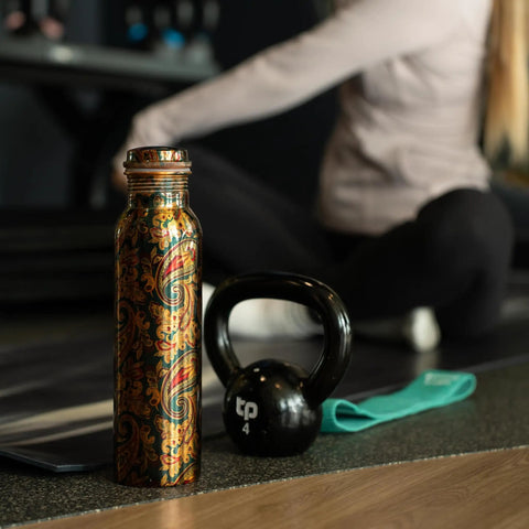 Copper Water Bottle 1 Liter With Ayurvedic Health Benefits beside gym equipment and person stretching.