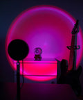 Sunset Lamp With Remote LED RGB Projection Night Light casting multicolor sunset glow in a living room with guitar in the background.