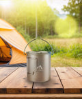 Pure Titanium 750ml Camping Pot With Spork Kit For Solo Backpacking on a wooden table near a tent, ideal for outdoor cooking.