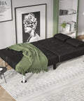 Futon Sofa Bed Convertible Lounge With Adjustable Back Three Positions 120 160 180 Degrees Removable Armrests Two Cup Holders PU Leather Black in a Cozy Living Room Sleep Solution setup as a bed with a green blanket.