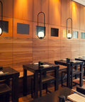 Capri 7 Inch Integrated LED Pendant Light in Black with White Glass Shade over dining tables in modern restaurant setting.