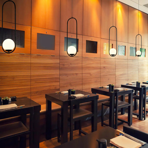 Capri 7 Inch Integrated LED Pendant Light in Black with White Glass Shade over dining tables in modern restaurant setting.