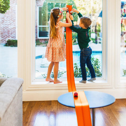 Two children playing with Flexible 15 Foot Race Car Track For Kids With Suction Cups Rolls Up Portable Racetrack on window.