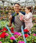 Adult and child in garden holding plant and watering can amidst flowers, suitable for Pink Kids Gardening Tools Set With Rake Shovel Trowel.