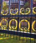 Decorative black and yellow wrought iron gate with circular patterns in a garden setting.