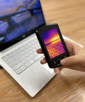 Hand holding Pocket Thermal Camera With 160x120 Infrared Resolution near laptop, showing thermal image on 3.5 inch screen.