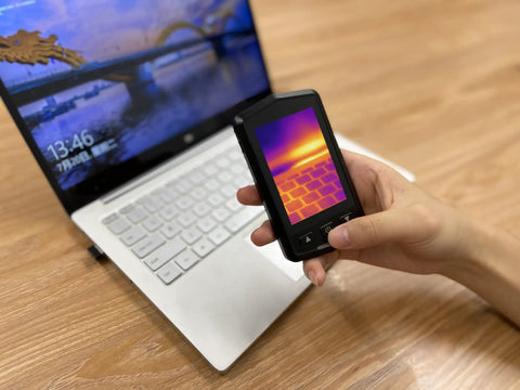Hand holding Pocket Thermal Camera With 160x120 Infrared Resolution near laptop, showing thermal image on 3.5 inch screen.