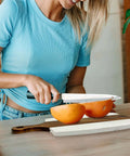 Marble-and-wood cutting board with handle; person slices orange halves on kitchen counter
